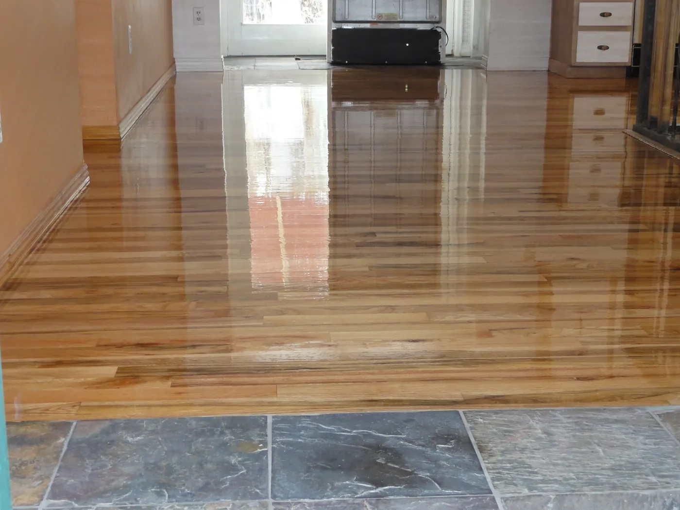 High gloss refinished hardwood floor reflecting windows beside a slate tile transition
