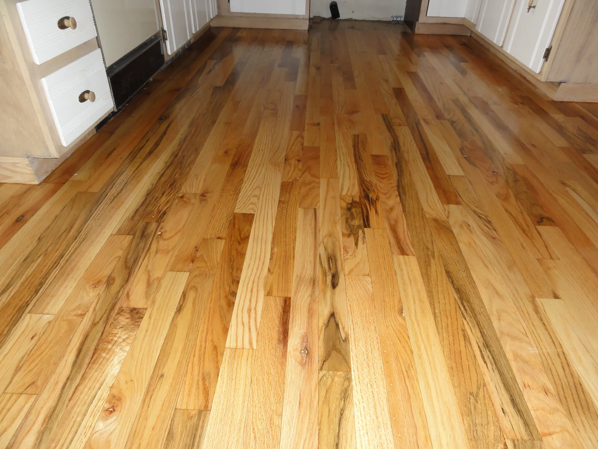 Oak plank floor with natural knots and color variation running toward a kitchen